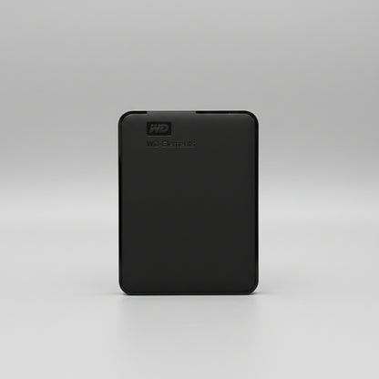 A black Western Digital WD Elements portable external hard drive standing upright on a wooden tabletop against a white paneled wall.